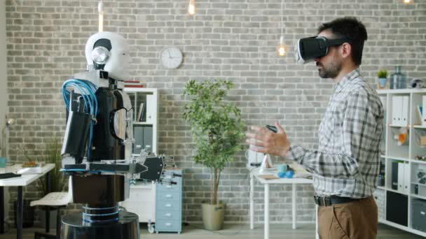 Zijaanzicht van de ontwikkelaar in virtual reality glazen bewegende hand en robot herhalen — Stockvideo