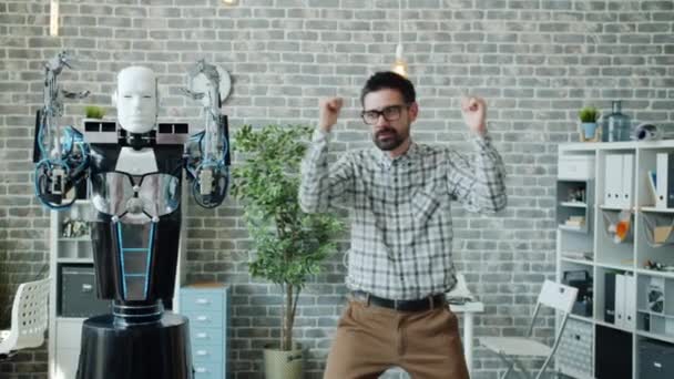Wesoły pracownik biurowy tańczy z robotem w pracy bawiąc się podczas przerwy — Wideo stockowe