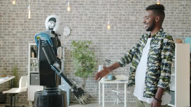 Vista lateral do empresário afro-americano feliz apertando a mão para cyborg inteligente — Vídeo de Stock
