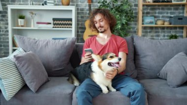 Yakışıklı adam akıllı telefon kullanıyor ve evdeki kanepede mantar sosisi okşuyor.