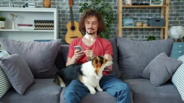 Adam mantar yavrusunu okşayıp evdeki kanepede dinlenirken akıllı telefon kullanıyor.