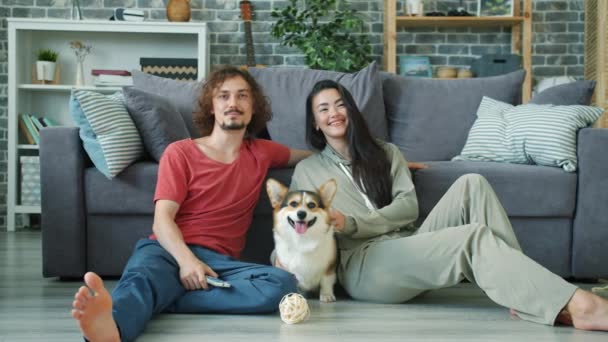 Pasangan bahagia gadis dan pria menonton TV dan memeluk corgi doggy di rumah — Stok Video