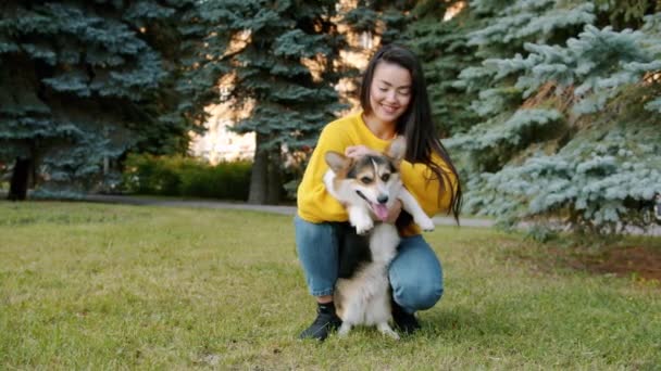 Αργή κίνηση του χαριτωμένο κορίτσι της Ασίας αγκαλιάζει corgi σκυλί στο πάρκο την ημέρα του φθινοπώρου — Αρχείο Βίντεο
