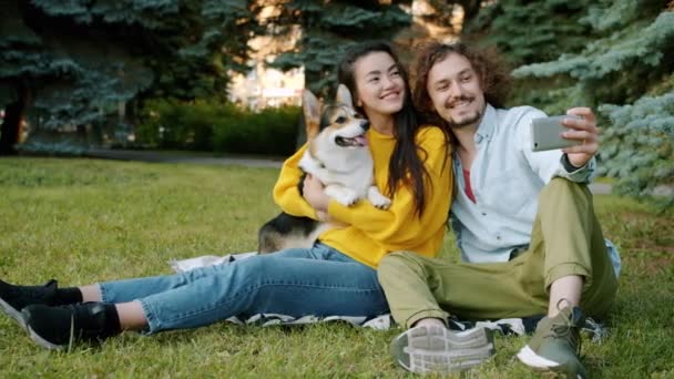 Dívka a chlap s selfie s corgi štěně pomocí smartphone v městském parku — Stock video