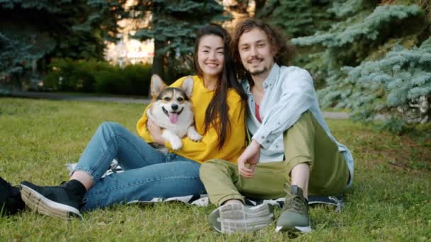 Retrato en cámara lenta de pareja joven y perro corgi sonriendo relajándose en el parque — Vídeo de stock