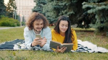 Kız kitap okurken adam akıllı telefon kullanıyor. Şehir parkında dinleniyor.