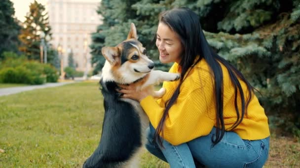 Cámara lenta de chica asiática abrazando y besando corgi perro al aire libre en parque de la ciudad — Vídeo de stock