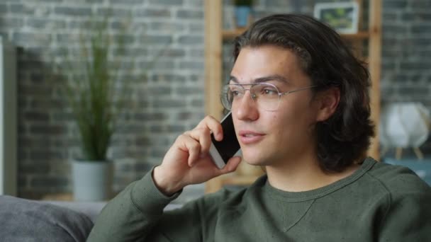 Радостный студент разговаривает по мобильному телефону в квартире наслаждаясь разговором — стоковое видео