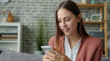 Akıllı telefon mesajları kullanan çekici genç bir kadın dairede eğleniyor.