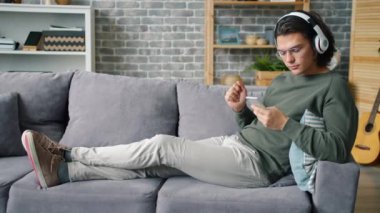 Yakışıklı adam kulaklıkla müzik dinliyor ve evdeki akıllı telefon ekranına dokunuyor.