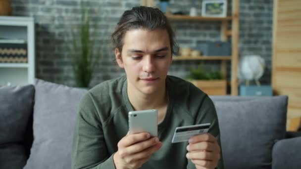 Joven hombre haciendo pago en línea con tarjeta bancaria tocando la pantalla del teléfono inteligente — Vídeos de Stock