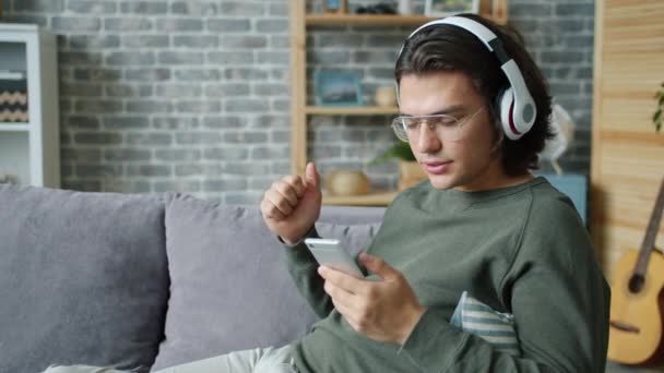 Cámara lenta de la persona alegre escuchando música en casa y usando un teléfono inteligente — Vídeos de Stock
