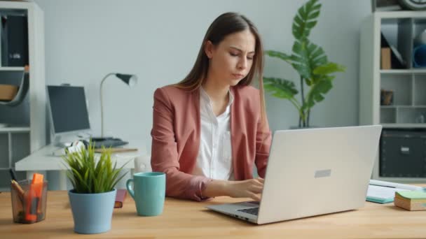 Виснажений офісний працівник гарна дівчина використовує ноутбук, а потім торкається голови почуття втоми — стокове відео