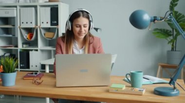 Yaratıcı ofis çalışanı kulaklıkla müzik dinliyor ve dizüstü bilgisayarla yazı yazıyor.