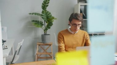 Erkek ofis çalışanı parlak çıkartmalı cam levhanın arkasında dizüstü bilgisayar kullanıyor.