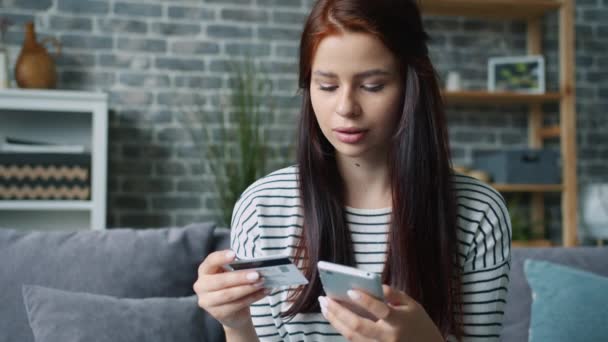Медленное движение счастливой женщины, которая платит онлайн банковской картой, используя смартфон дома — стоковое видео