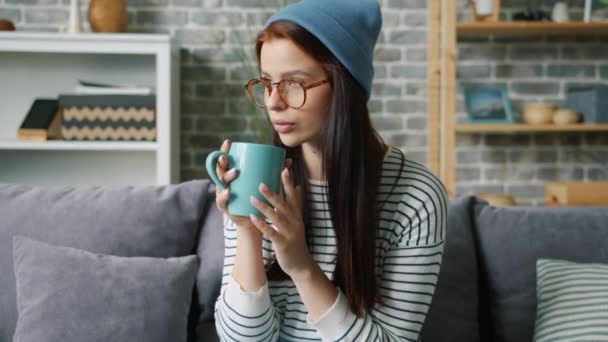 Cámara lenta de chica bonita en gafas de beber celebración taza en casa relajante — Vídeo de stock