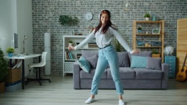 Kulaklık takan mutlu kadın dansçı dairede tek başına dans edip eğleniyor.