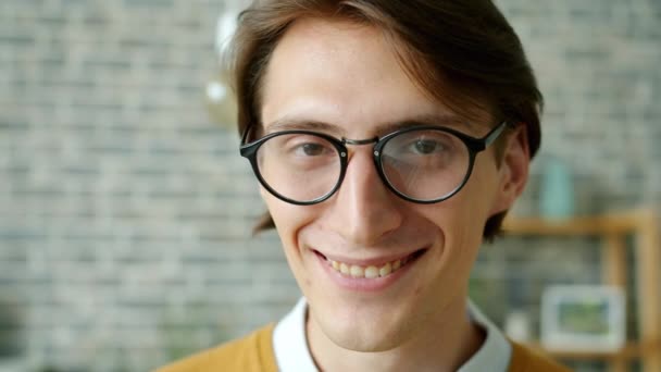 Retrato de cerca del joven en gafas de moda sonriendo de pie en casa — Vídeo de stock