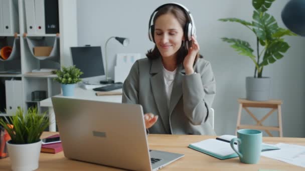 Speelse dame luisteren naar muziek in hoofdtelefoon dansen werken met laptop plezier hebben — Stockvideo