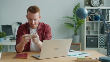 Yakışıklı adam modern ofiste rahat bir şekilde akıllı telefondan mobil video oyunu oynuyor.