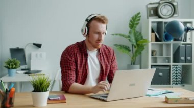 Kulaklık takan neşeli adam ofiste dans ediyor laptopla iş yapıyor.