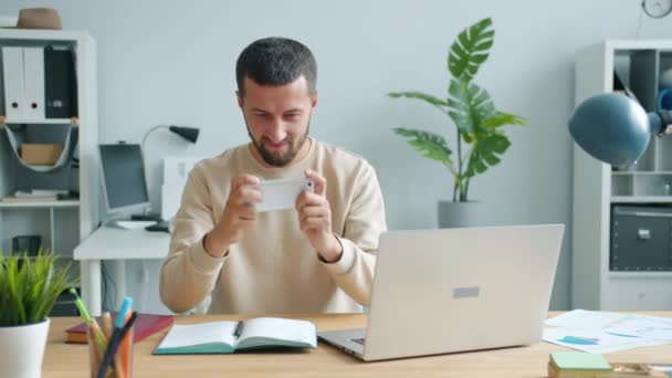 Trabalhador de escritório jogando jogo de smartphone relaxante durante a pausa no trabalho no local de trabalho — Vídeo de Stock