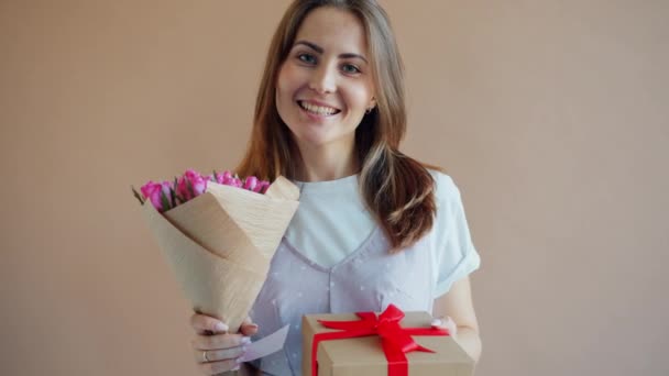 Portrait of happy young lady with flowers and gift box on beige background — Stock Video