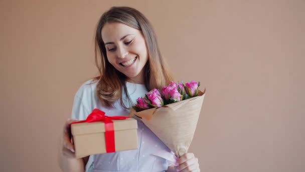 Porträtt av dam med massor av blommor och presentförpackning ler på beige bakgrund — Stockvideo