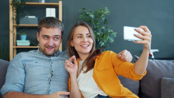 Мужчина и женщина делают селфи со смартфоном веселятся, смеясь, целуясь — стоковое видео