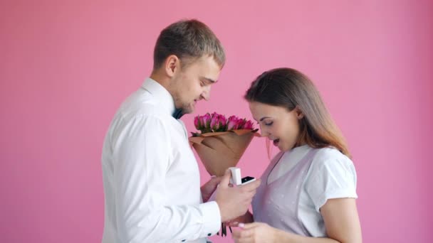 Mann in eleganter Kleidung schenkt fröhlicher junger Frau lächelnd Blumen und Ring — Stockvideo