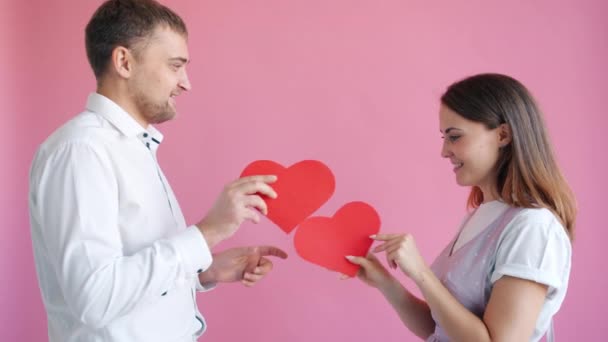 Man and woman exchanging heart shape valentine cards looking in the eye smiling — Stock Video