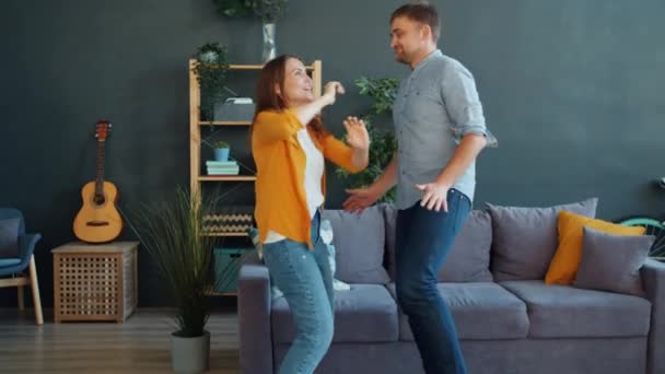 Mąż i żona tańczą razem w mieszkaniu ubrani w luźne ubrania i dobrze się bawią — Wideo stockowe