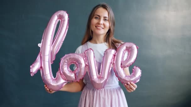 Beautiful woman holding English word love and smiling on gray background — Stock Video