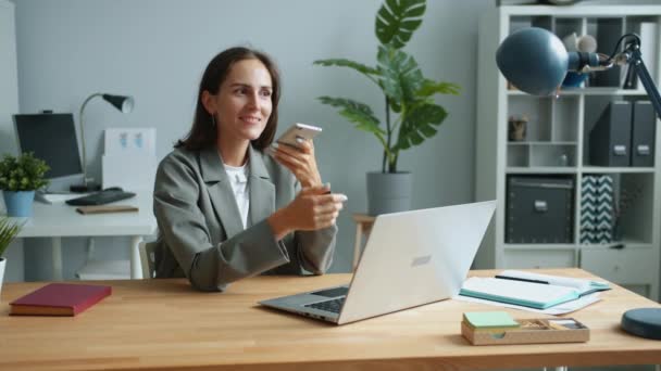 Young female office worker is recording audio message using smartphone — Stock Video