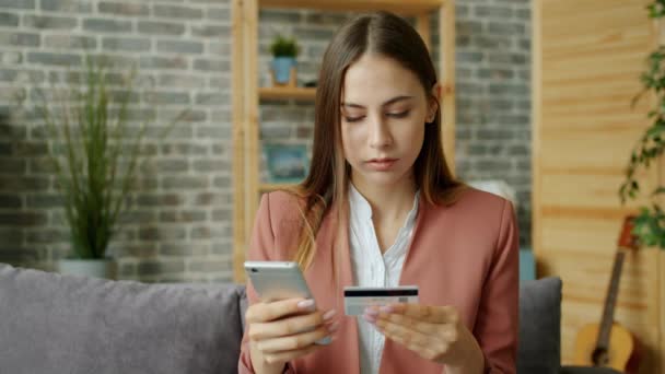 Молодая леди делает онлайн-платеж, держа банковскую карту и касаясь экрана смартфона — стоковое видео