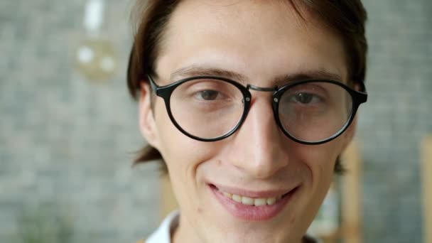 Retrato en cámara lenta de un chico atractivo con gafas sonriendo solo en casa — Vídeos de Stock