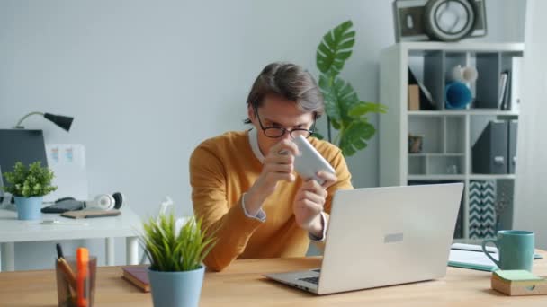 Trabalhador de escritório alegre jogando videogame na tela de toque do smartphone no local de trabalho — Vídeo de Stock