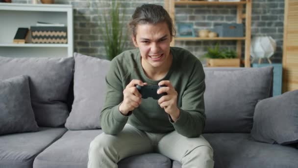 Emotionele jongeman spelen video game thuis zitten op de bank thuis — Stockvideo