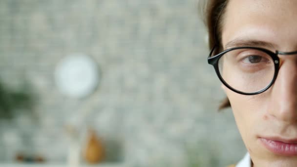 Close-up retrato de cara séria metade cara olhando para a câmera usando óculos em casa — Vídeo de Stock