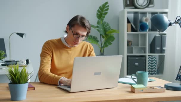 Веселый парень, использующий ноутбук, печатающий, работающий за столом в офисе, сосредоточен на работе — стоковое видео