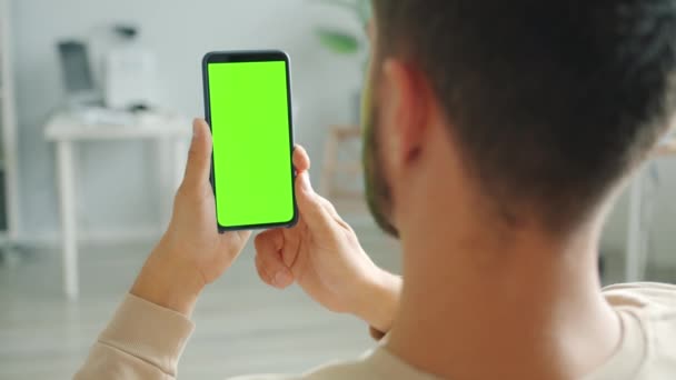 Trage beweging van man met behulp van smartphone met groen scherm in huis holding gadget — Stockvideo