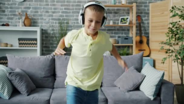 Retrato de niño alegre divirtiéndose en casa escuchando música en auriculares bailando — Vídeo de stock