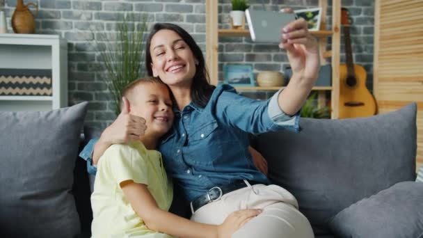 Älskade mamma tar selfie med bedårande son med hjälp av smartphone kamera kramar barn — Stockvideo