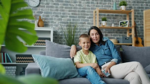 Mamá y el niño viendo la televisión juntos riendo hablando vinculación en apartamento moderno — Vídeo de stock