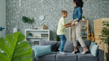 Neşeli çocuk. Aktif annesiyle kanepede zıplayıp evde birlikte eğleniyor.
