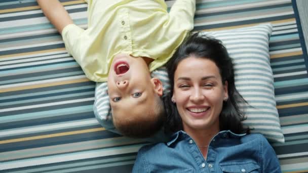 Porträtt av mor och son gör roliga ansikten liggande på golvet hemma ha kul — Stockvideo