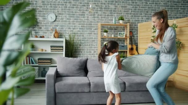 Mama i córka walczą poduszki zabawy w mieszkaniu śmiejąc się razem — Wideo stockowe