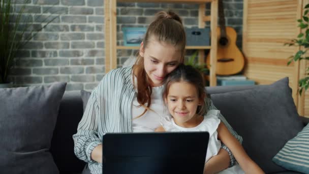 Μητέρα και κόρη χρησιμοποιούν φορητό υπολογιστή κοιτάζοντας την οθόνη απολαμβάνοντας την τεχνολογία στο σπίτι — Αρχείο Βίντεο