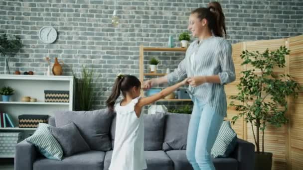 Χαρούμενο κορίτσι που χορεύει με τη νεαρή αστεία μητέρα στο σπίτι και χοροπηδάει χαλαρώνοντας μαζί — Αρχείο Βίντεο
